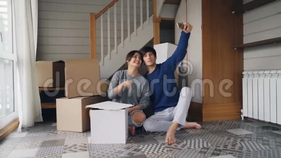 幸福的家庭夫妻正在自拍房子的钥匙坐在新公寓的地板上靠近纸箱视频的预览图