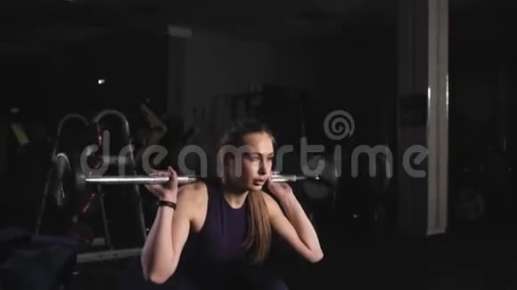 运动型健身女孩用杠铃做深蹲运动健身房的晚间训练视频的预览图
