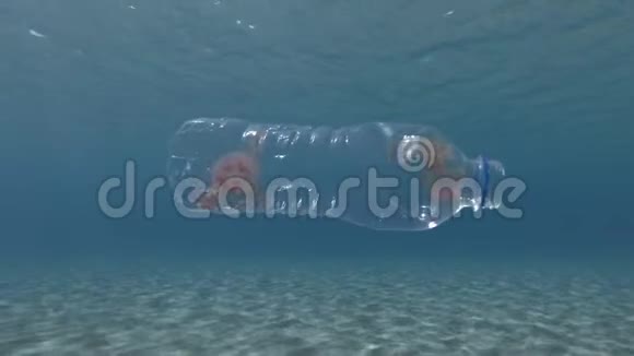 塑料污染果冻鱼在塑料瓶中缓慢地漂浮在阳光下的蓝色水面下视频的预览图