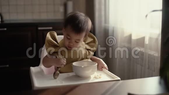 穿绿色围兜的小女孩正用勺子从桌子上吃婴儿粥视频的预览图