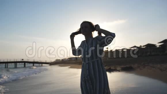 一个年轻女子张开双臂旋转的剪影女孩在海滩上的阳光下兴奋地旋转视频的预览图