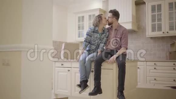 年轻的接吻夫妇坐在新公寓的厨房桌子上一家人搬到一个新家带着一个视频的预览图