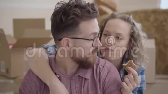 漂亮女人吃饼干的肖像从背后拥抱戴眼镜的胡子男人未包装的箱子在视频的预览图