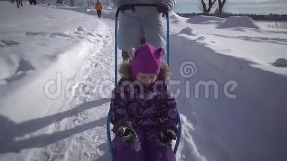 一个年轻的女人骑着一个小女孩在冬天公园的一条小路上雪橇视频的预览图