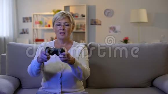 快乐成熟的女士按下游戏机按钮玩电子游戏坐在家里沙发视频的预览图