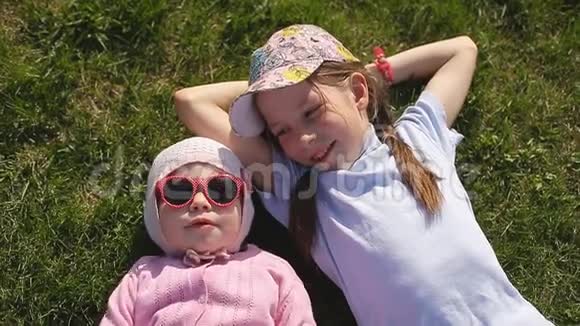 在一个阳光明媚的日子里两个妹妹躺在绿草上一个戴棒球帽另一个戴针织帽子戴红色视频的预览图