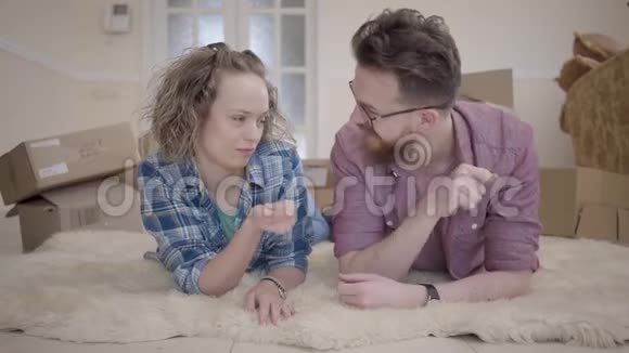 年轻的家庭躺在蓬松的地毯上背景上有盒子男人手里藏着钥匙但她视频的预览图