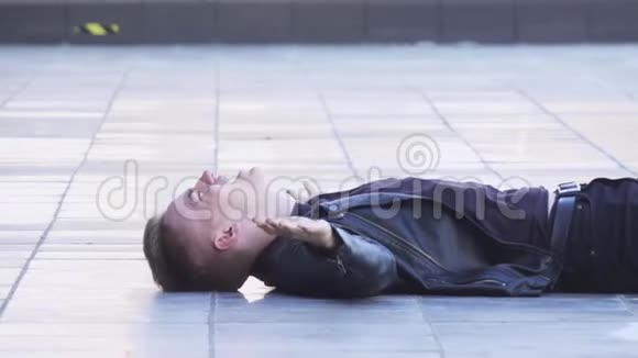 迷人的年轻金发男性穿着黑色夹克躺在白色瓷砖地板上视频的预览图