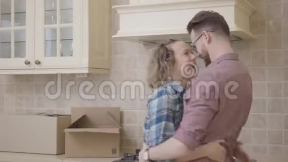 欢乐的年轻家庭拥抱在厨房在他们的新家幸福的一对夫妇搬到了一间新公寓视频的预览图