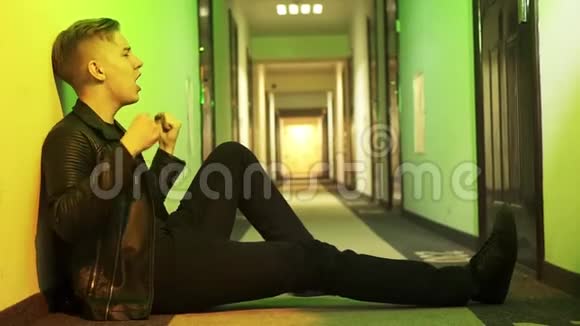 穿着夹克发型漂亮的帅哥坐在走廊的地板上唱歌视频的预览图