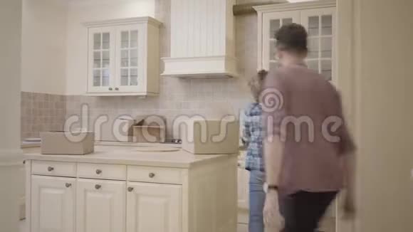 快乐的年轻家庭在他们的新家的厨房里闲逛幸福的一对夫妇搬到了一间新公寓丈夫视频的预览图