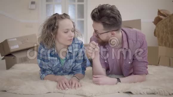 年轻的家庭躺在蓬松的地毯上背景上有盒子男人给妻子钥匙人们微笑着视频的预览图