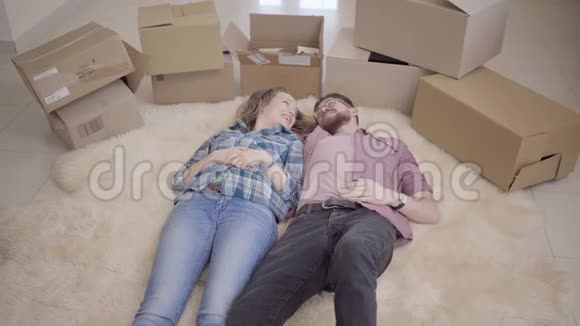 一对年轻的夫妇躺在地板上旁边有许多盒子男人和女人说话躺在蓬松的地毯上已婚视频的预览图