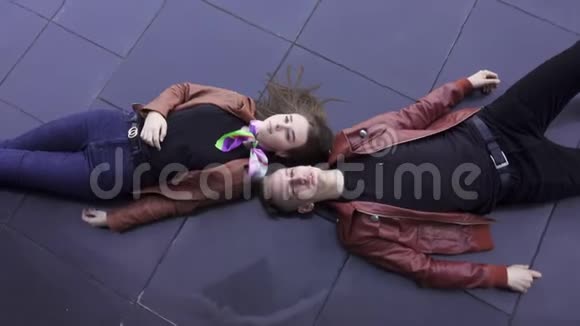 年轻的金发歌唱的男人和漂亮的女人穿着浅棕色的夹克躺在瓷砖地板上视频的预览图