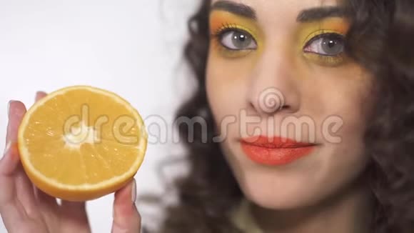 特写年轻卷曲女孩的肖像与明亮的化妆舔成熟多汁的橘子与乐趣视频的预览图