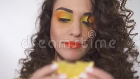 特写一幅可爱的年轻卷发女孩的肖像她的妆容鲜艳咬着一片多汁的橘子视频的预览图