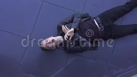 好看的年轻金发男人穿着黑色夹克唱歌躺在瓷砖地板上视频的预览图