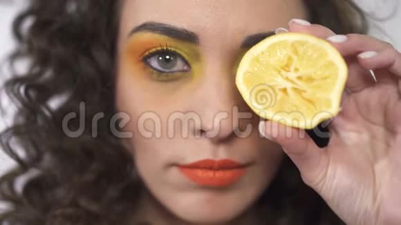 特写俏皮的年轻卷曲女孩的肖像微笑着用圆形的成熟柠檬遮住眼睛慢动作视频的预览图