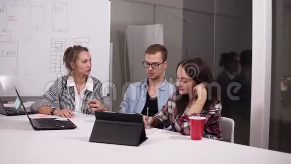 业务团队讨论项目或想法戴眼镜的年轻人和两个随意坐在办公室桌上的女人视频的预览图