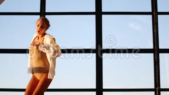 一个年轻而精力充沛的女孩跳着卑鄙的舞蹈在一个有大的全景窗户的阁楼工作室里一个穿着一身衬衫的女人视频的预览图