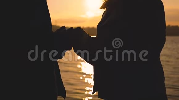 一对可爱的夫妇的夜晚剪影站在湖边夕阳西下视频的预览图