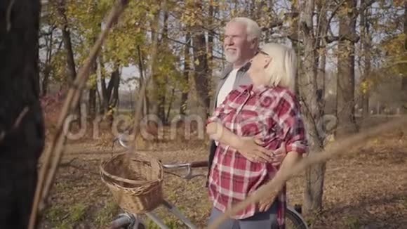 快乐的白种人退休夫妇站在秋天的森林或公园阳光下拥抱的肖像成熟成熟视频的预览图