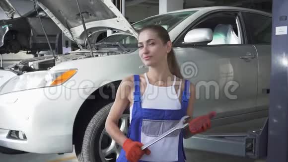 车间起重机械和汽车背景下的年轻女专业汽车技工扳手画像视频的预览图