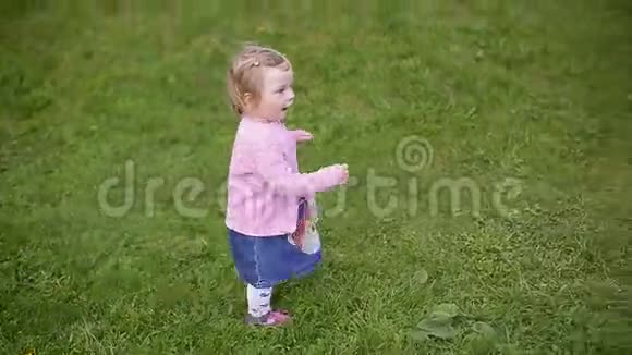 小二岁美丽的金发女孩穿过绿草慢动作视频视频的预览图