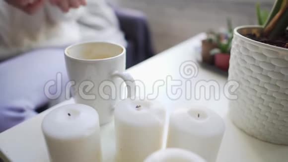 在一张白色的桌子上放上蜡烛和咖啡杯女孩在热饮中加入棉花糖以保持温暖和享受视频的预览图