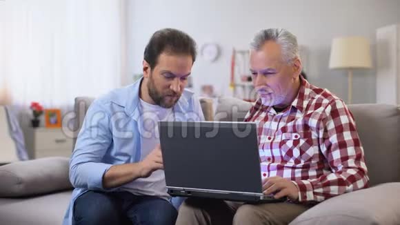年轻的儿子向父亲解释如何使用笔记本电脑现代技术设备视频的预览图