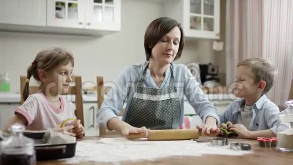 妈妈教孩子们如何在厨房的桌子上用面团做饼干视频的预览图