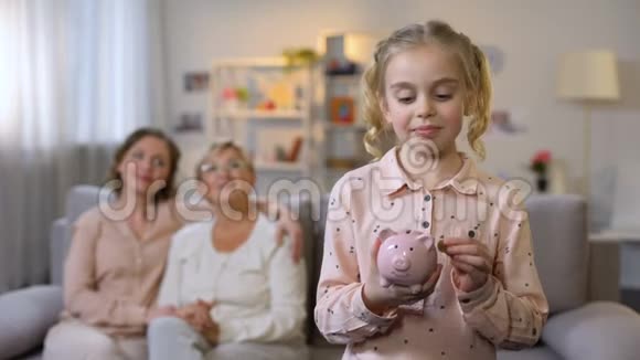 女孩子放硬币储蓄罐奶奶和妈妈坐在后面储蓄视频的预览图