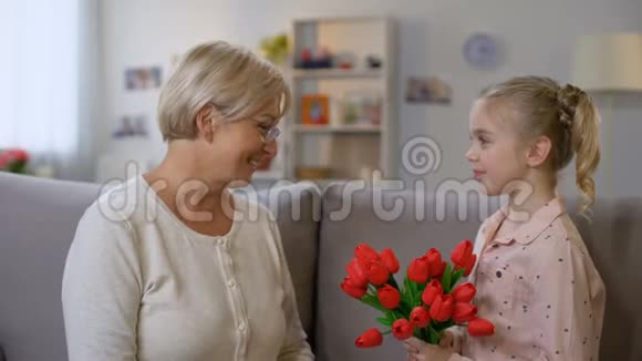可爱的女孩把红色郁金香送给祖母和拥抱家人的爱生日视频的预览图