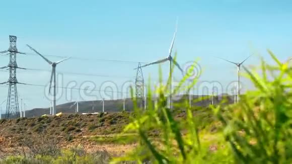 风车发电机的涡轮机绿色灌木植物在前景高压电力线路概念视频的预览图