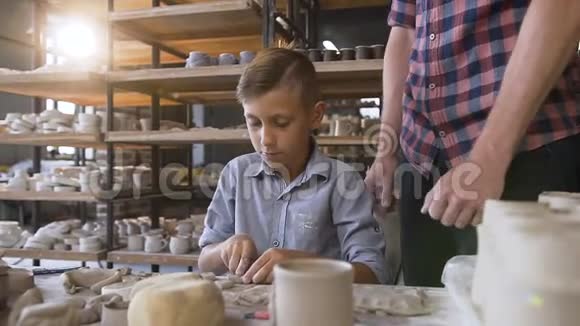 可爱的父亲教小儿子如何在陶工轮上用粘土工作视频的预览图