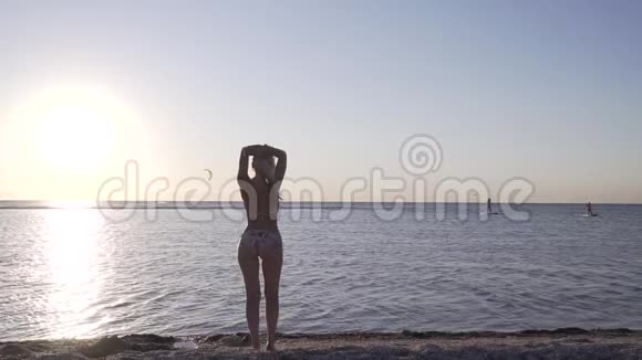 年轻女子站在海边的水边摆着五颜六色的日落视频的预览图