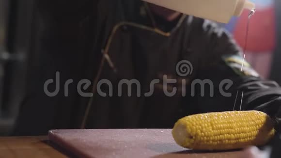 厨师用糖浆把玉米头和骨头倒在玉米头上把瓶子举得很高用黑色长袍和橡胶手套做饭视频的预览图