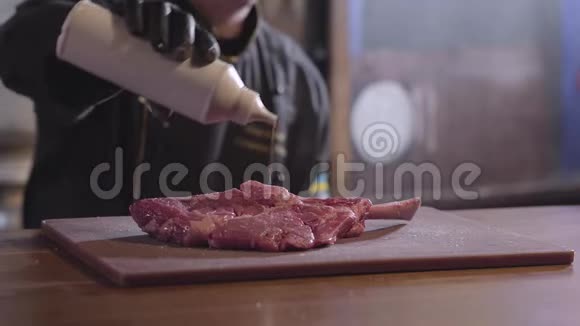 厨师倒一块带骨头的肉两边都贴着糖浆用黑色长袍和橡胶手套烹饪视频的预览图