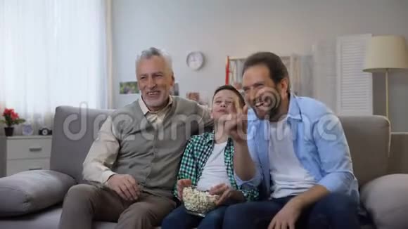 快乐的爷爷爸爸和儿子一起享受电视上的喜剧节目视频的预览图