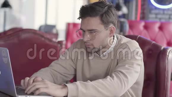 帅哥在现代咖啡馆里用笔记本电脑工作时髦自信的商人有节奏地移动他的身体视频的预览图