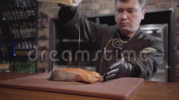 肖像厨师倒大片三文鱼与油接近穿黑色长袍和橡胶手套的人做菜准备视频的预览图