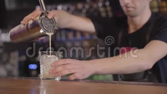 酒吧老板用冰块把金属摇床上的鸡蛋鸡尾酒倒入杯子里把它变成一个圆圈做美味鸡尾酒的年轻人视频的预览图