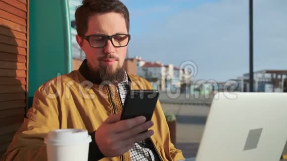 男人在户外观看智能手机屏幕手提电脑和咖啡视频的预览图