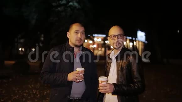 晚上两个男人在街上喝着纸板杯里的咖啡聊天视频的预览图