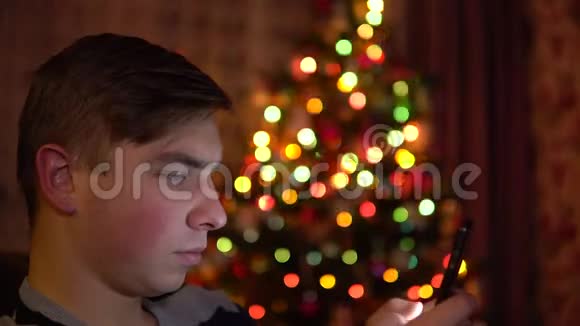 一个年轻人坐在圣诞树的背景上手里拿着一块平板电脑整个房间都是装饰的视频的预览图