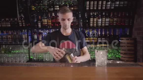 专业的酒保把鸡尾酒放在一个摇床上站在酒吧柜台上放在瓶子的背景上视频的预览图