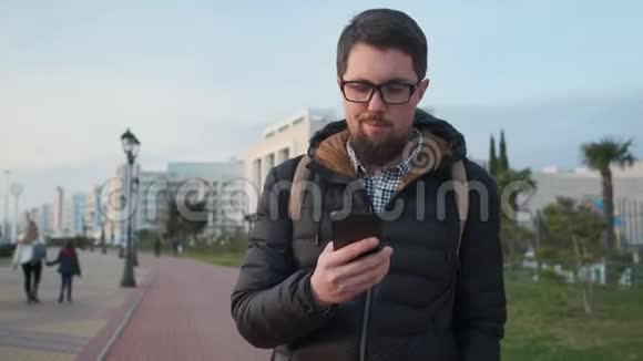 大胡子男人在城市里散步在智能手机里看短信视频的预览图