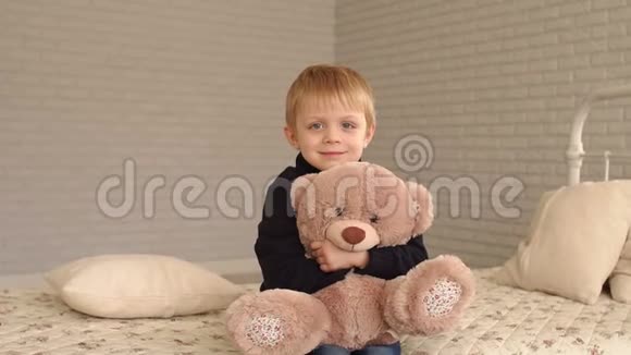 一个金发小男孩在家里和他最喜欢的泰迪熊在床上的肖像视频的预览图