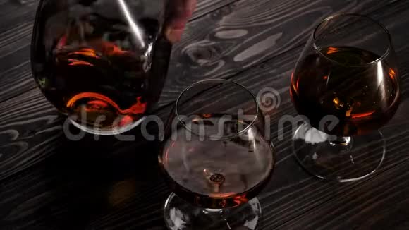 豪华白兰地手把圆瓶放在木桌上两个玻璃杯附近白兰地白兰地嗅探器狂欢慢动作视频的预览图
