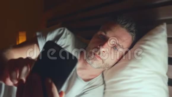 年轻迷人放松的男人在家中的横向围拍深夜用手机在床上联网视频的预览图